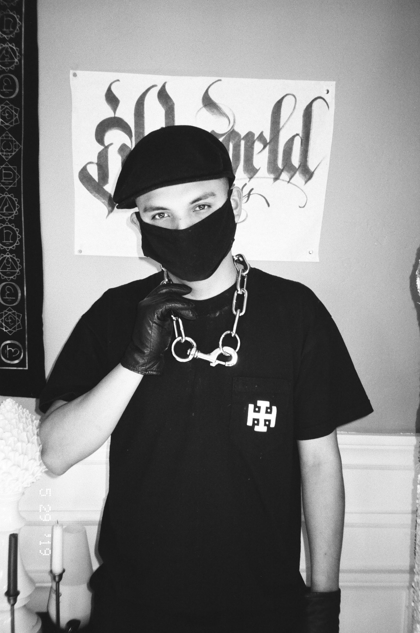 Person wearing a black mask and gloves with a black t-shirt featuring a logo,