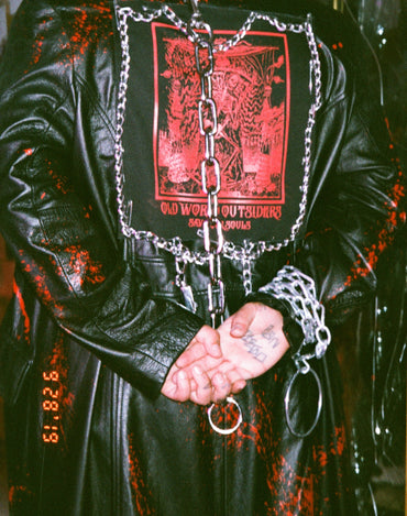 Person wearing a black leather outfit with chains and a red graphic on a dark background