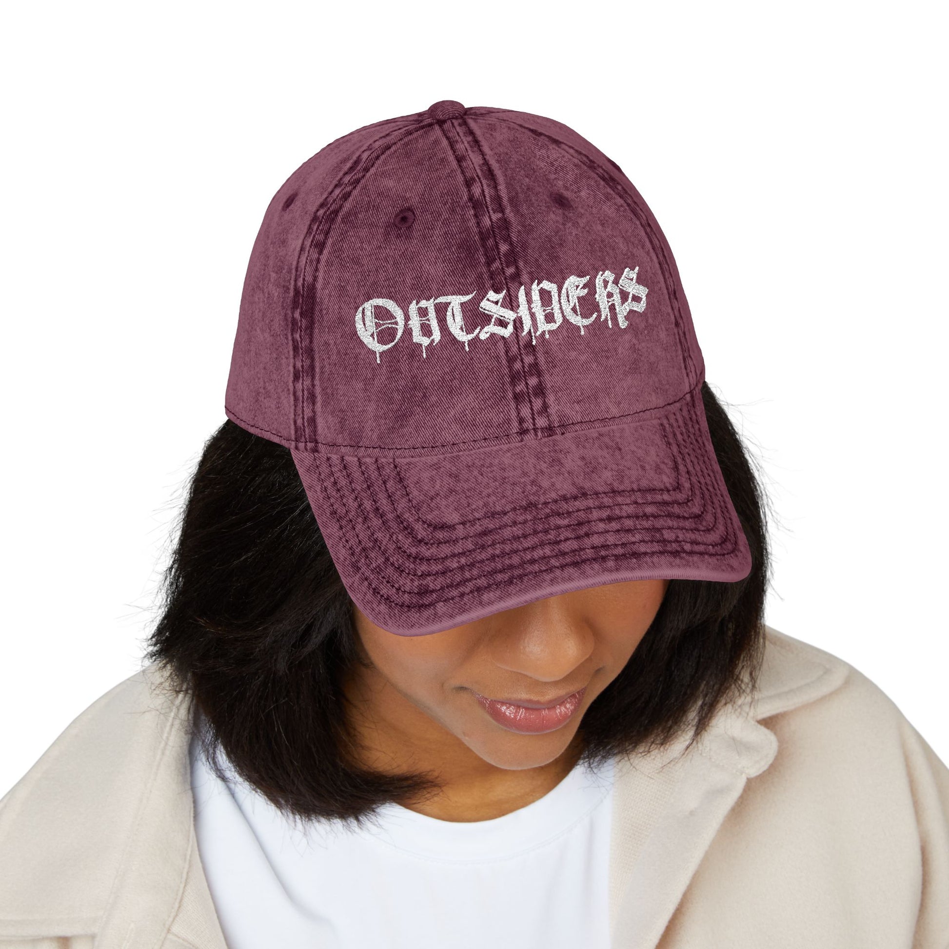 Person wearing a maroon cap with 'Outsiders' text on a white background