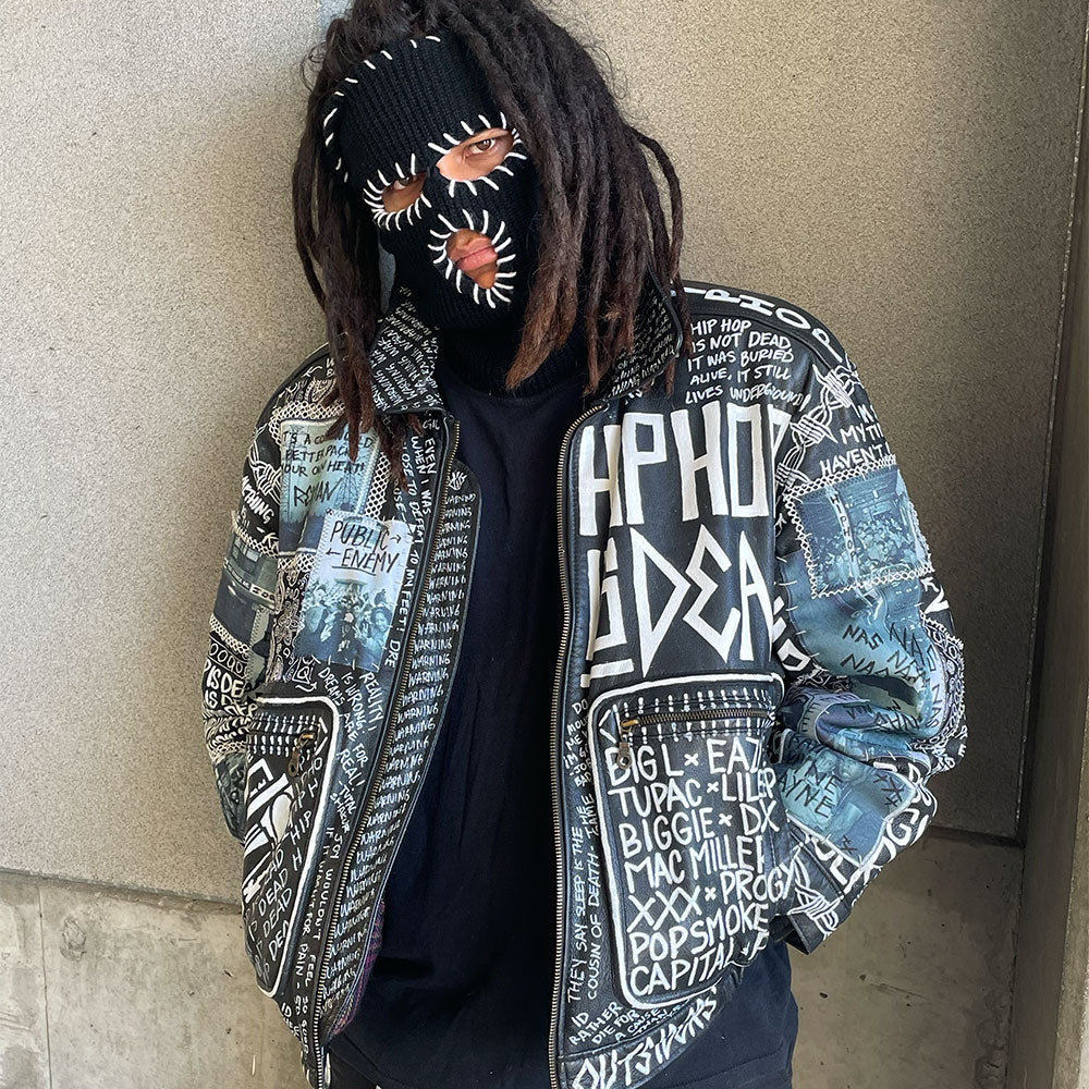 Person wearing a jacket with text and graphics, standing against a plain wall.