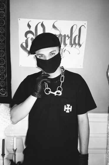 Person wearing a black mask and gloves with a black t-shirt featuring a logo, 