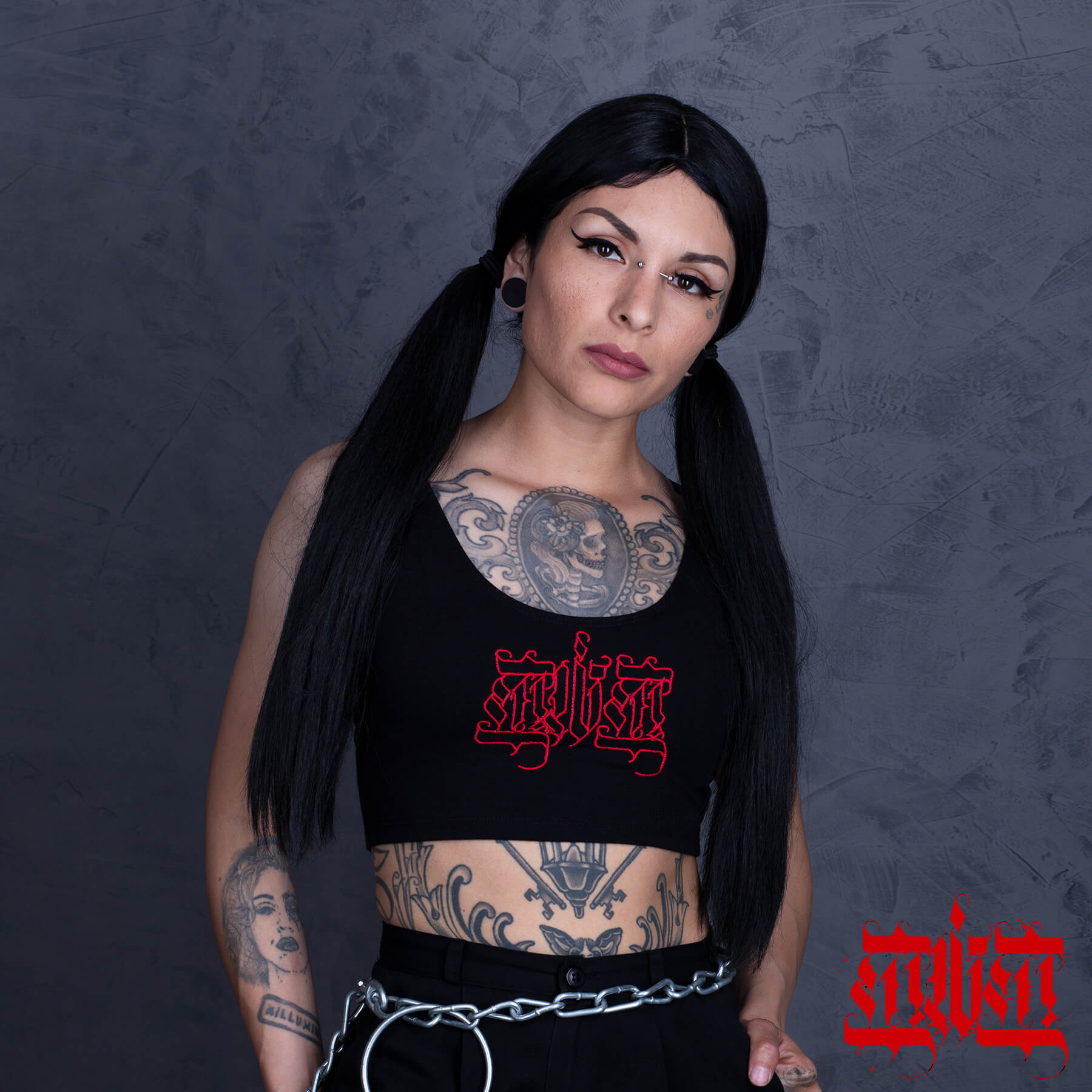 Woman with tattoos wearing a black crop top with red text against a dark background
