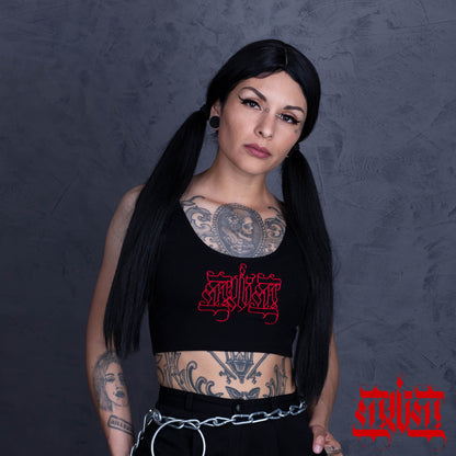 Woman with tattoos wearing a black crop top with red text against a dark background