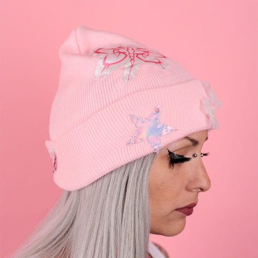 Person wearing a pink beanie with decorative elements on a pink background