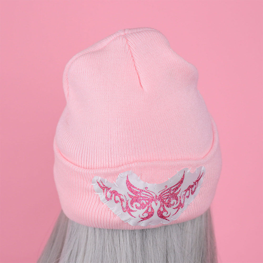 Pink beanie with a decorative emblem on a pink background