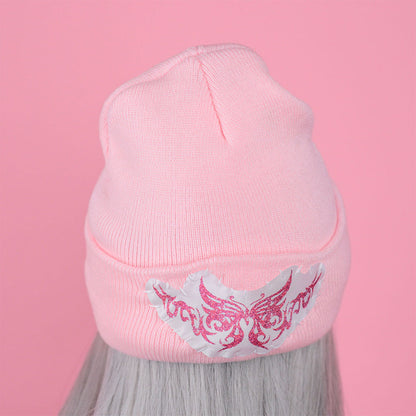 Pink beanie with a decorative emblem on a pink background