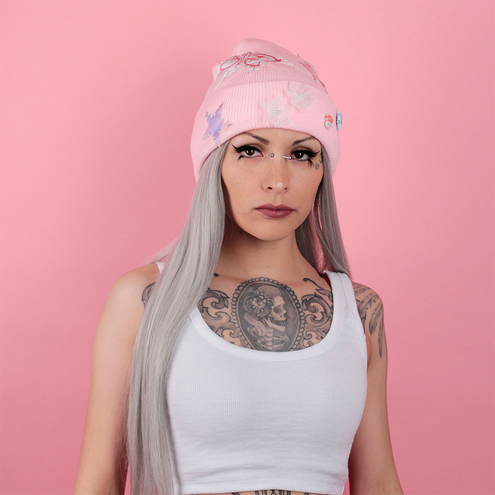 Woman wearing a pink beanie with butterfly designs on a pink background