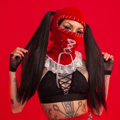 Person wearing a red mask and black outfit with tattoos on a red background