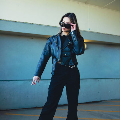 Woman wearing a blue leather jacket and black pants standing in an underpass.